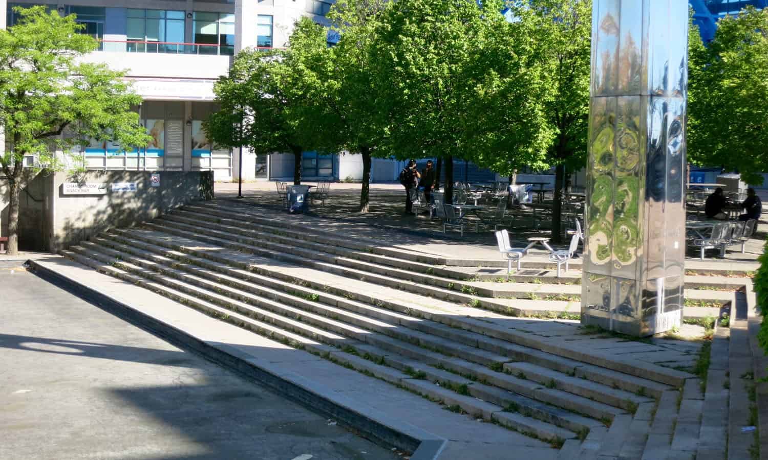 A grove of trees, outdoor seating, a tower, and a cascade of steps descending to the reflecting pool in Albert Campbell Square